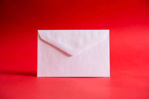 Witte envelop op rode achtergrond, om een liefdesbrief te schrijven op Valentijnsdag voor uw partner, of om te veroveren. Het begrip liefde - Foto, afbeelding