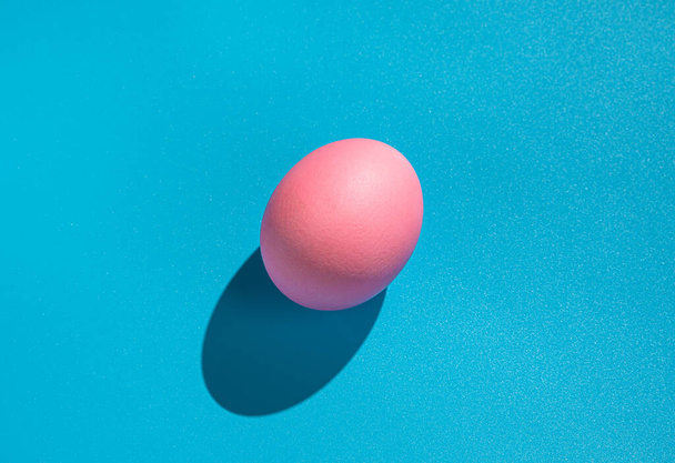 Uovo rosa su sfondo blu con un'ombra dura. Il concetto di Pasqua, cibo minimalista. - Foto, immagini