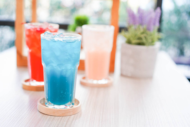 Verfrissende koude drank voor de zomer op ijs. Kleurrijke zomer drankje in hoog glas met houten schotel voor warme dag en feest. - Foto, afbeelding