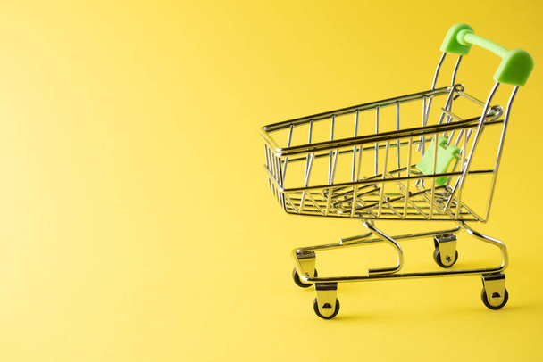 Close-up of green shopping carts on a yellow background. Sales concept. Cart, products, copy space. Side view - Photo, Image
