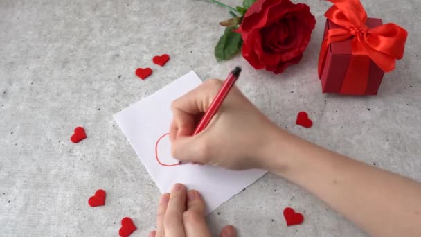 Mulher atrai um coração para a celebração de 14 de fevereiro. Corações, rosa e caixa de presente vermelho na mesa - Filmagem, Vídeo