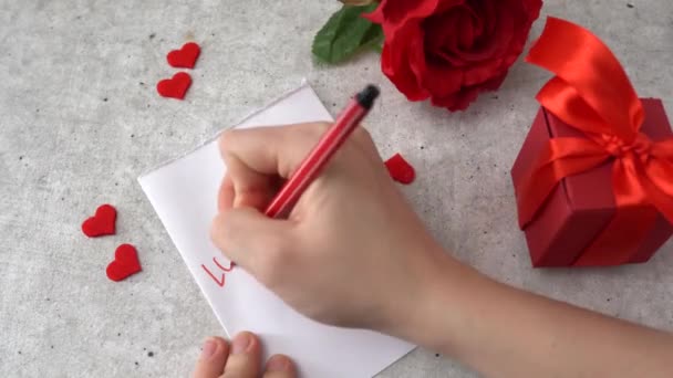Γυναίκα γράφει μασάζ Love You για 14 Φεβρουάριος γιορτή. Καρδιές, τριαντάφυλλο και κόκκινο κουτί δώρου στο τραπέζι - Πλάνα, βίντεο