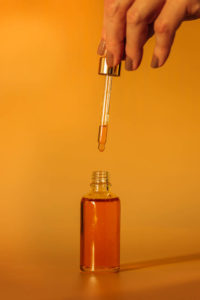 χέρι κρατώντας ένα μπουκάλι λάδι σε ένα γυάλινο βάζο σε κίτρινο φόντο - Φωτογραφία, εικόνα