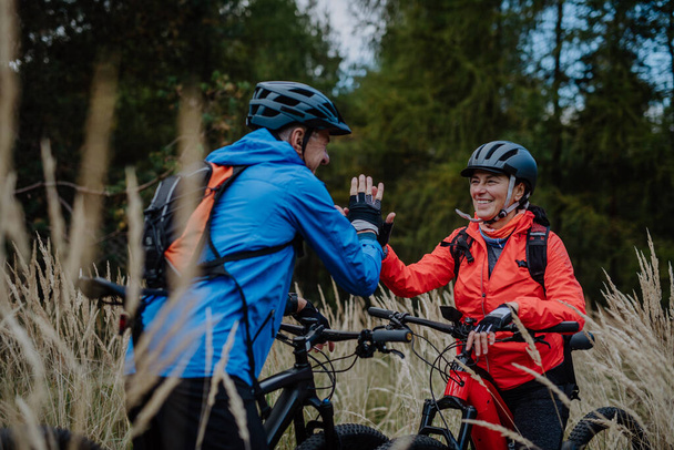 Senior couple bikers high fiving outdoors in forest in autumn day. - Foto, Imagen