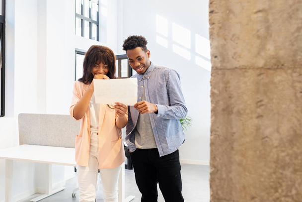 African woman and man standing in an office analyzing data on a sheet of paper. People working in co-working space - Photo, Image