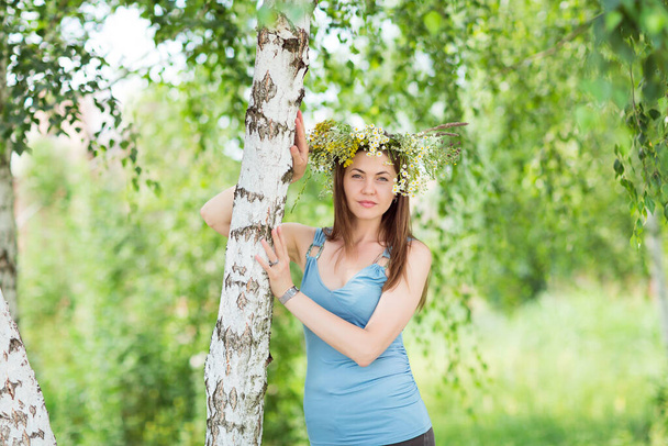 Pretty young woman with a flower wreath on her head in a forest - Фото, изображение