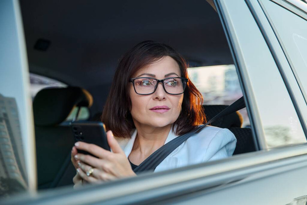 Portrait of middle-aged business woman in car in back passenger seat. - Fotografie, Obrázek