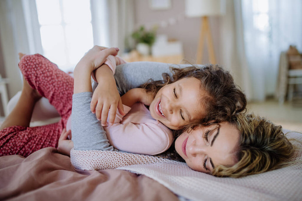 Onnellinen äiti makaa sängyllä pienen tyttärensä kanssa ja koteloituu kotona. - Valokuva, kuva