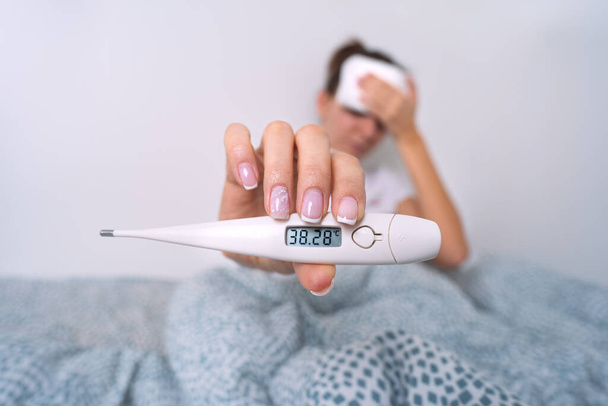 Nemocná žena s vysokou horečkou ukazující lékařský teploměr s teplotou 38,2. Žena měří tělesnou teplotu - Fotografie, Obrázek