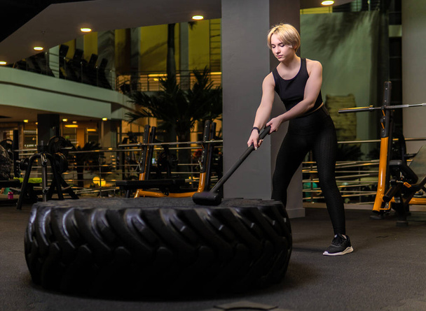 Wheel with sledgehammer girl stands tire gym exercise, from sport strong from bodybuilder young lifestyle, holding leaning. Braids muscles brunette, dark - Photo, Image