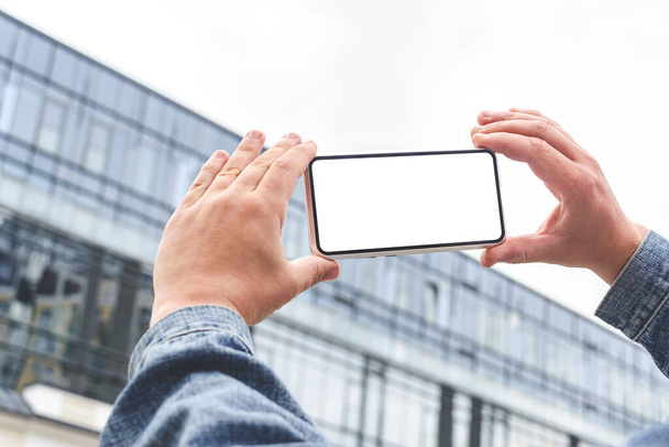 Smartphone-Attrappe in den Händen eines Mannes. Vor dem Hintergrund eines gläsernen Business Centers - Foto, Bild