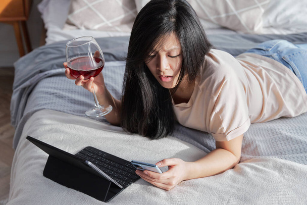 Poważna kobieta w luźnych ciuchach rozmawiająca przez wideo rozmowę na tablecie cyfrowym leżącym na łóżku - Zdjęcie, obraz
