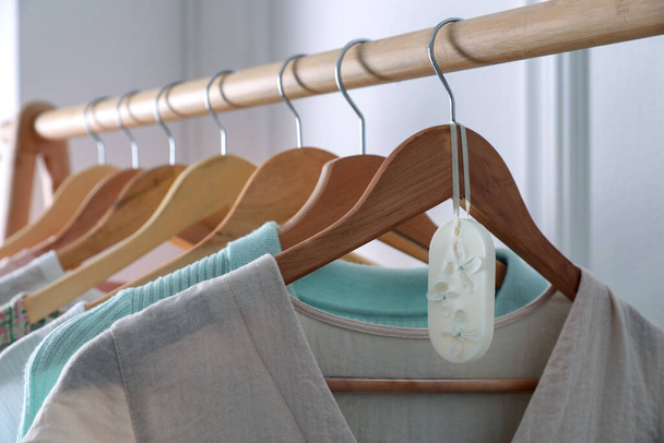 Beautiful scented wax sachet and clothes hanging on wooden rack indoors - Foto, Imagen