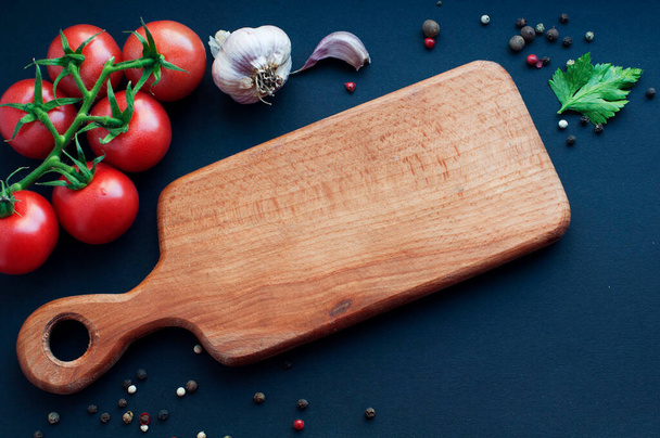 Empty wooden board with food ingredients on black background. Garlic, tomatoes, spices, pepper, parsley around wooden board - Valokuva, kuva