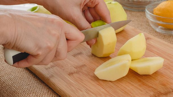 Woman cuts fresh peeled apples on a wooden cutting board on rustic background - Foto, afbeelding