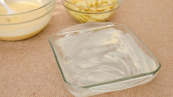 Mantequilla de vidrio bandeja para hornear de cerca en la mesa de la cocina. Proceso de cocción, receta de pastel de manzana. - Foto, imagen