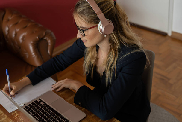 Молода жінка працює вдома з ноутбуком і паперами на столі і навушники. Концепція домашнього офісу. Сірий блокнот для роботи. Високоякісна фотографія
 - Фото, зображення