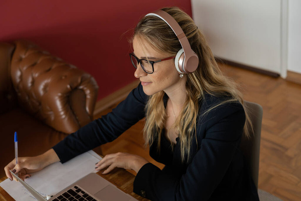 Young woman working at home with laptop and papers on desk and headphones.  Home office concept. Gray notebook for working. High quality photo - Foto, Bild
