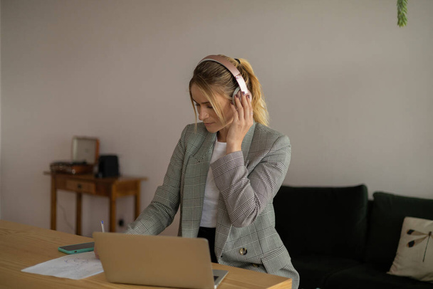 Egy fiatal nő, aki otthon dolgozik laptoppal, papírokkal és fejhallgatóval. Otthoni iroda koncepció. Szürke jegyzetfüzet a munkához. Kiváló minőségű fénykép - Fotó, kép