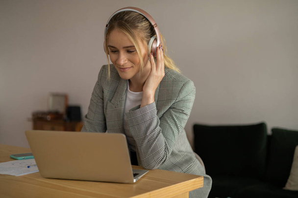Nuori nainen työskentelee kotona kannettava tietokone ja paperit pöydällä ja kuulokkeet. Pääkonttorin konsepti. Harmaa muistikirja työntekoon. Laadukas kuva - Valokuva, kuva
