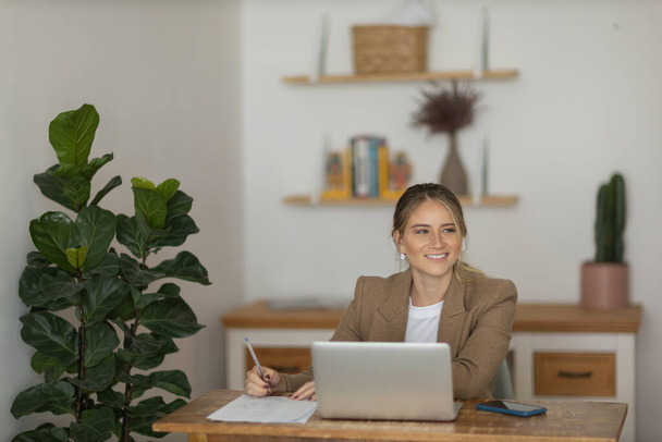 Een jonge vrouw die thuis werkt met een laptop en papieren op haar bureau in haar slaapkamer. Het concept van thuiskantoor. Grijze notitieblok voor het werk. Hoge kwaliteit foto - Foto, afbeelding