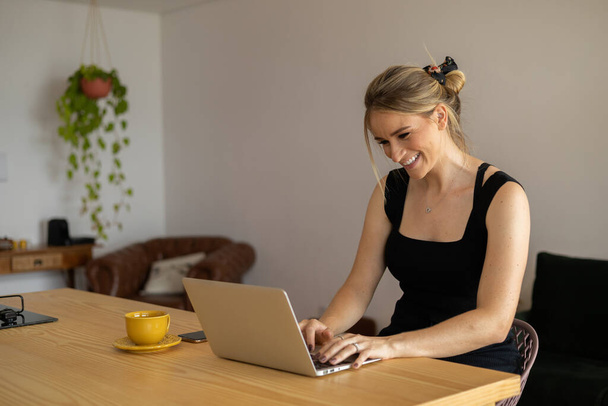 Young woman working at home in her kitchen with laptop and papers on kitchen wooden desk. Home office concept. Gray notebook for working. Home office concept. High quality photo - Fotó, kép
