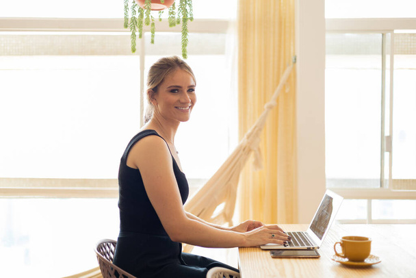 Mutfakta dizüstü bilgisayarı ve mutfak masasında kağıtlarıyla çalışan genç bir kadın. Merkez ofis konsepti. Çalışmak için gri defter. Merkez ofis konsepti. Yüksek kalite fotoğraf - Fotoğraf, Görsel