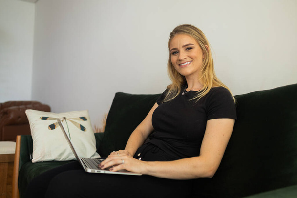 自宅のリビングルームのソファでノートパソコンを膝の上で作業している若い女性。内務省の概念。仕事のための灰色のノート。内務省の概念。高品質の写真 - 写真・画像