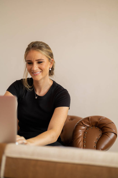 Young woman working at home with laptop on a brown arm chair with a white background. Home office concept. Gray notebook for working. Home office concept. High quality photo - Φωτογραφία, εικόνα