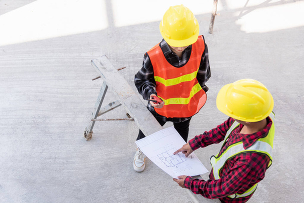 Architect and client discussing help create plan with blueprint of the building at construction site floor. Asian engineer foreman worker man and woman meeting and planning construction work, top view - Zdjęcie, obraz
