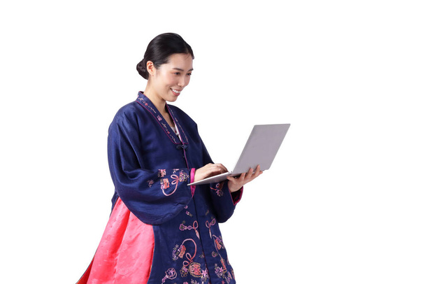 Mooie Aziatische vrouw draagt hanbok, de nationale jurk van Korea. Staan met een laptop op een witte achtergrond. geïsoleerd. Knippad - Foto, afbeelding