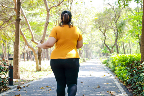 Sarı bluz giyen şişman Asyalı kadın sabah parkta koşuyor. Şişman insanların sağlığı için kilo verme egzersizi kavramı. Boşluğu kopyala - Fotoğraf, Görsel
