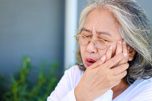 Asiatische ältere Frau hat Zahnschmerzen Legen Sie Ihre Hand über den Mund. Das Konzept der Mundgesundheit von Senioren. Alterskrankheiten. Rentenversicherung - Foto, Bild