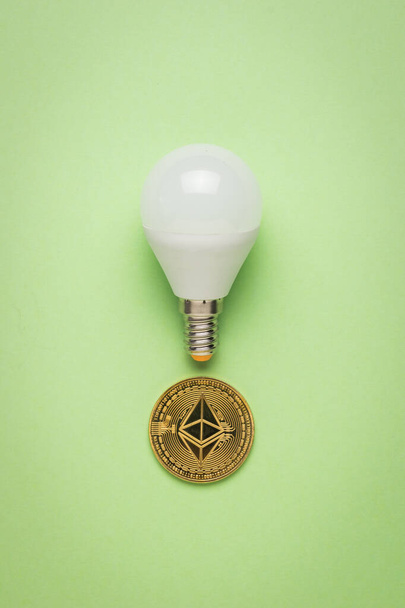 Lampada a LED e moneta digitale su sfondo verde chiaro. Il concetto di pagamenti per l'elettricità in moneta digitale. - Foto, immagini