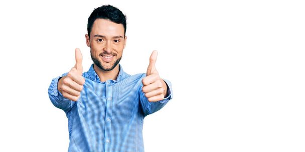 Hispanic man with beard wearing casual business shirt approving doing positive gesture with hand, thumbs up smiling and happy for success. winner gesture.  - Photo, Image