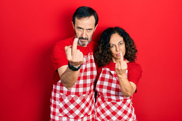 Middle age couple of hispanic woman and man wearing cook apron showing middle finger, impolite and rude fuck off expression  - Φωτογραφία, εικόνα