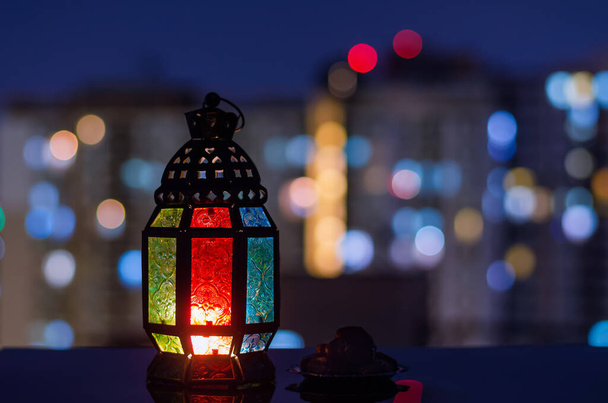 Linterna y pequeño plato de dátiles de frutas con el edificio de apartamentos de fondo para la fiesta musulmana del mes santo de Ramadán Kareem. - Foto, imagen