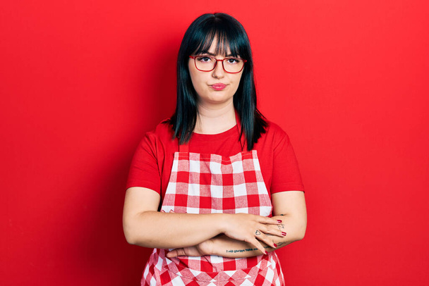 Young hispanic woman wearing cook apron and glasses skeptic and nervous, disapproving expression on face with crossed arms. negative person.  - Photo, Image
