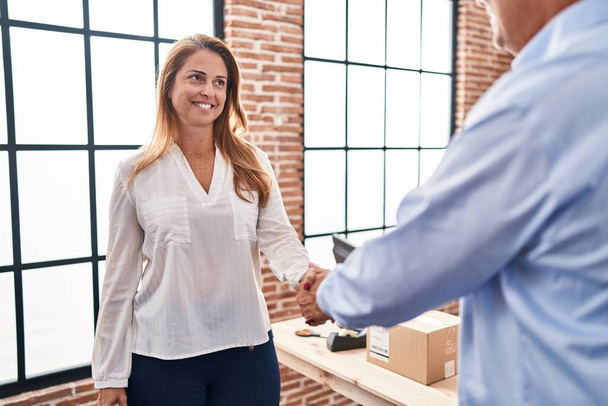 Мужчины и женщины среднего возраста, работающие в электронной торговле, пожимают друг другу руки в офисе - Фото, изображение