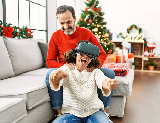 Középkorú spanyol pár mosolyog boldog ül a kanapén játszik virtuális valóság szemüveg otthon. - Fotó, kép