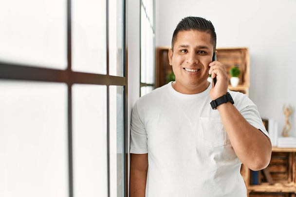 Jovem hispânico sorrindo feliz falando no smartphone em casa. - Foto, Imagem