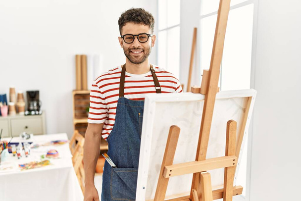 Арабський молодий чоловік в художній студії з радісною і прохолодною посмішкою на обличчі. Щаслива.  - Фото, зображення