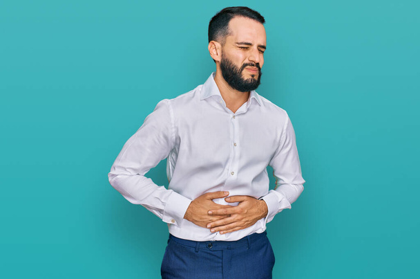 Young man with beard wearing business shirt with hand on stomach because nausea, painful disease feeling unwell. ache concept.  - 写真・画像