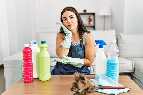 Nuori brunette nainen yllään puhtaampaa esiliina ja käsineet puhdistus kotona ajattelu näyttää väsynyt ja kyllästynyt masennus ongelmia ristissä kädet.  - Valokuva, kuva