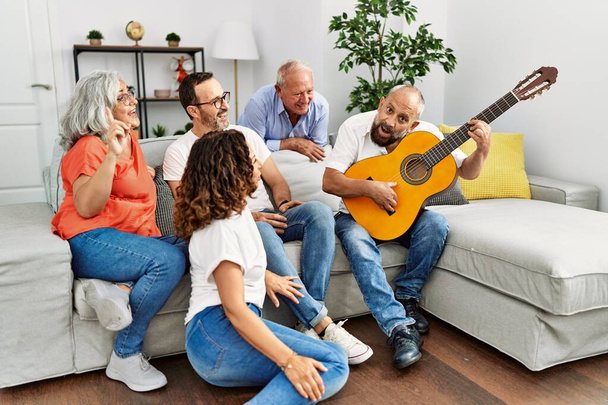 Gruppe von Freunden mittleren Alters bei einer Party mit klassischer Gitarre zu Hause auf dem Sofa sitzend. - Foto, Bild