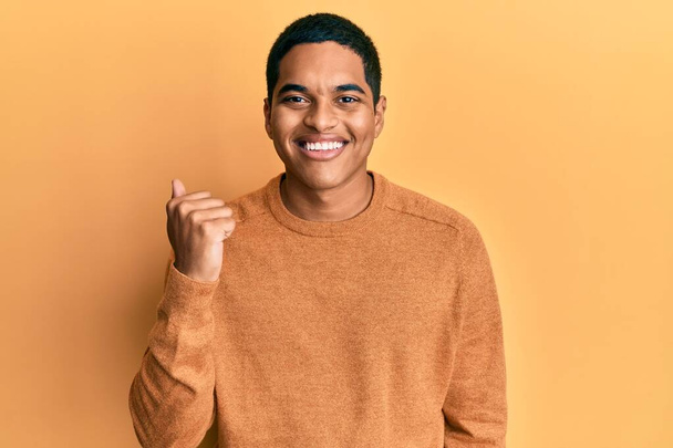 Joven hombre hispano guapo vistiendo suéter casual de invierno sonriendo con la cara feliz mirando y señalando a un lado con el pulgar hacia arriba.  - Foto, imagen