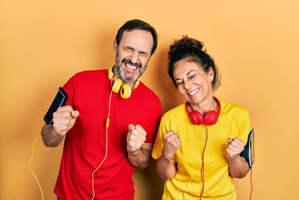 Middle age couple of hispanic woman and man wearing sportswear and arm band excited for success with arms raised and eyes closed celebrating victory smiling. winner concept.  - Photo, Image