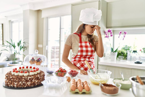 Mooie jonge brunette gebak chef-kok vrouw koken gebak in de keuken moe wrijven neus en ogen gevoel vermoeidheid en hoofdpijn. stress en frustratie concept.  - Foto, afbeelding