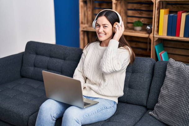 Jovem mulher usando laptop e fones de ouvido sentados no sofá em casa - Foto, Imagem