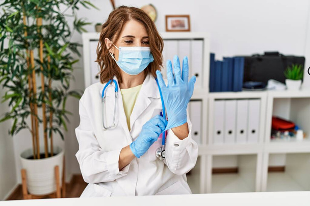 Middle age hispanic woman wearing doctor uniform and medical mask at clinic - Photo, Image